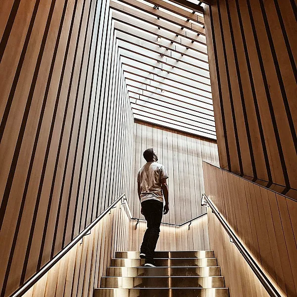 Un hombre mira hacia el techo de listones de madera desde la parte superior de una escalera dentro del Audain Art Museum