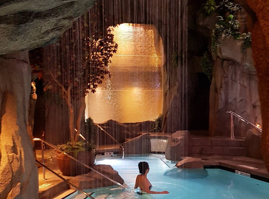 A women dips into an underground pool at the Tigh-Na-Mara Grotto Spa. The water is bright blue and the walls are carved out from rock.