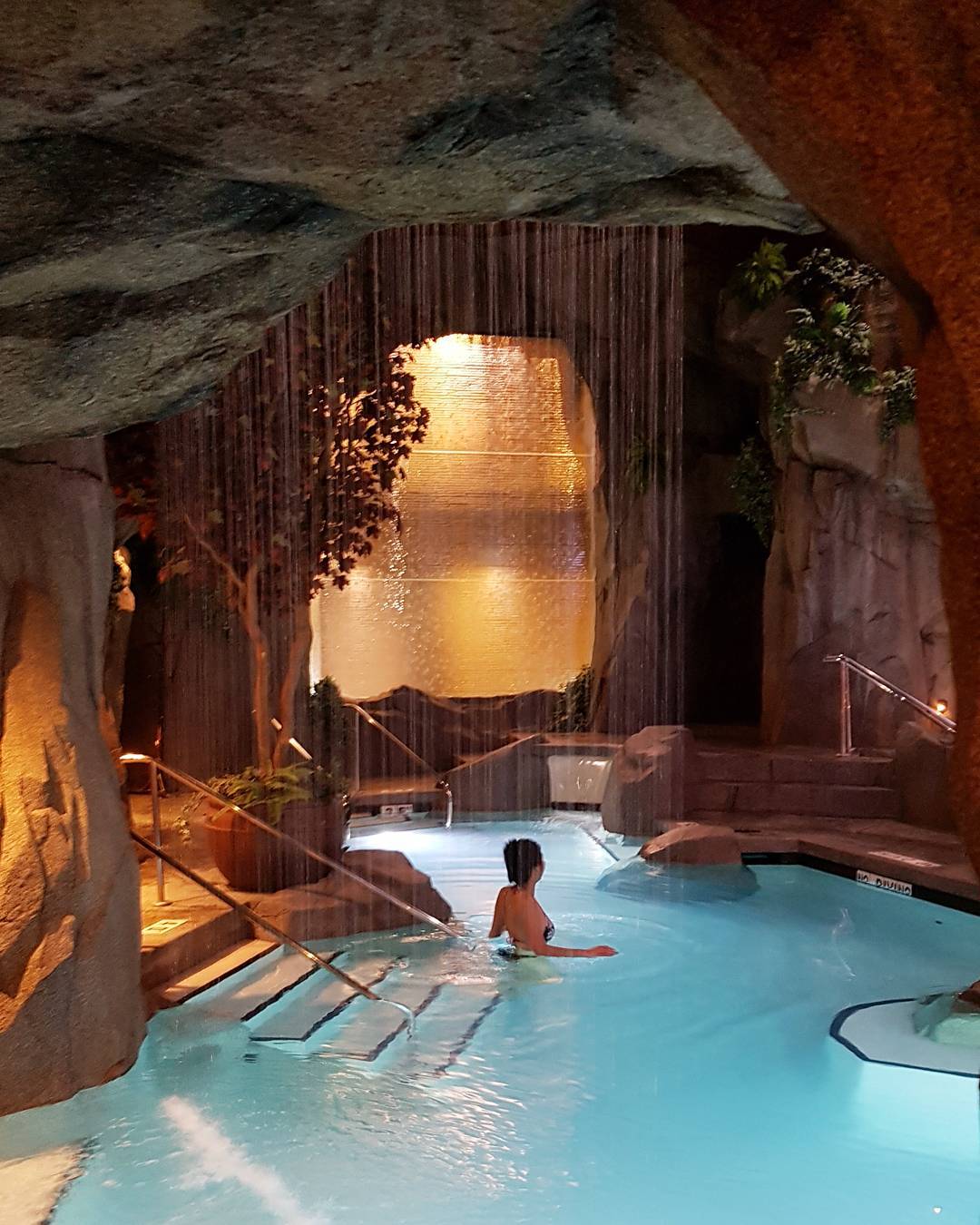 A women dips into an underground pool at the Tigh-Na-Mara Grotto Spa. The water is bright blue and the walls are carved out from rock.