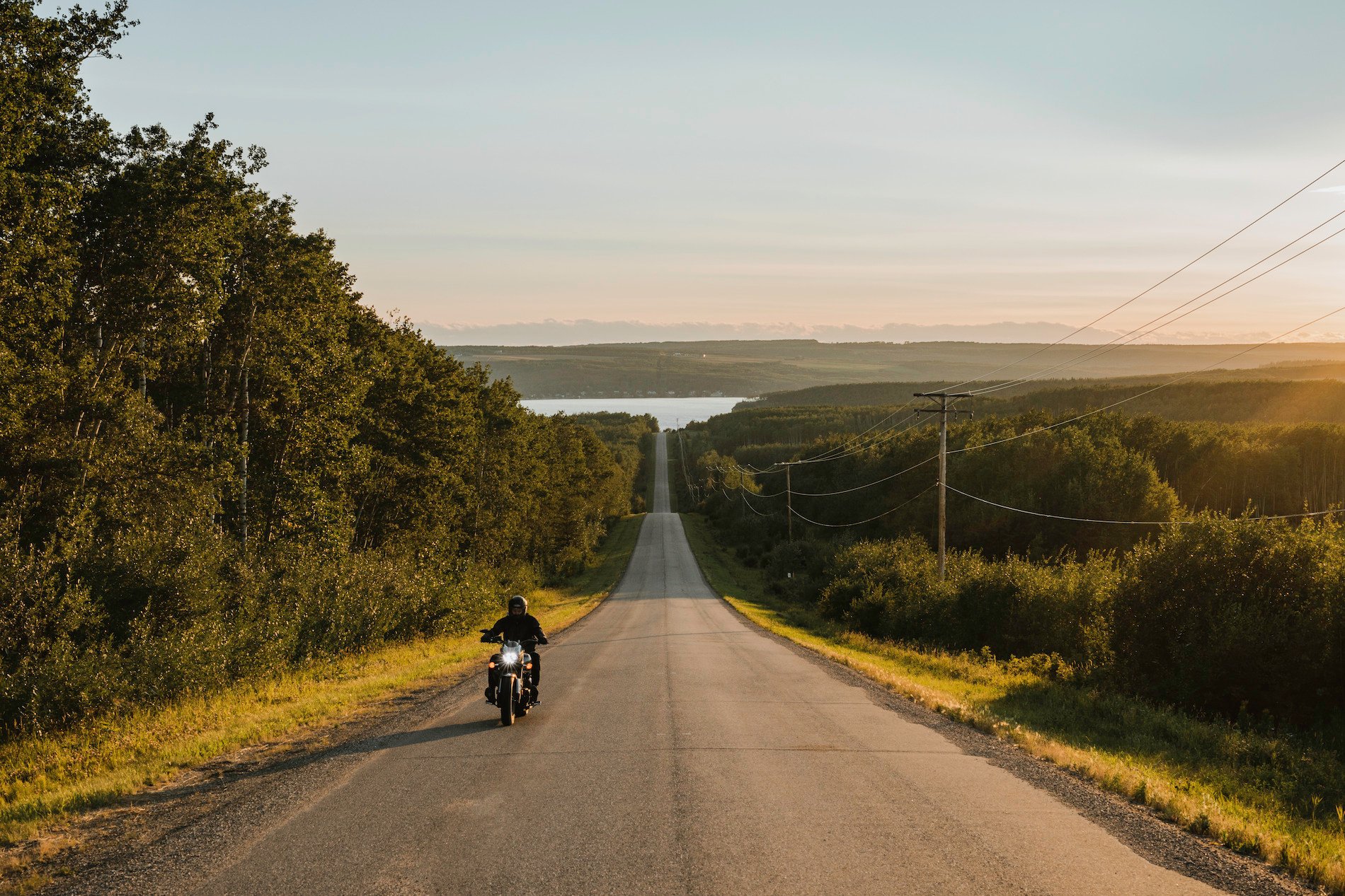 A motorocycle drives along a country road lined by foliage near Fort St. John.