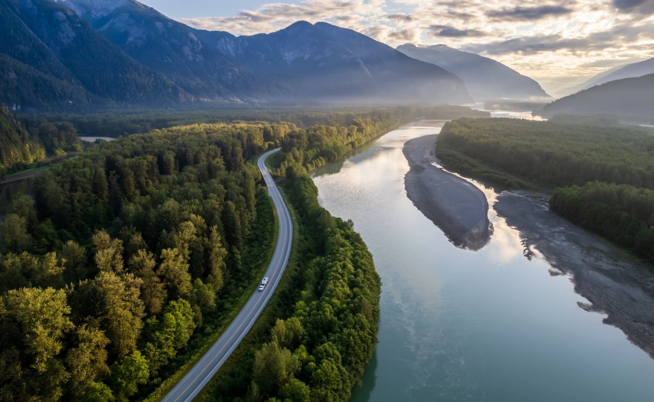 Ein Wohnmobil schlängelt sich über einen Highway, umgeben von dichtem Wald, hohen Bergen und einem ruhigen Fluss.