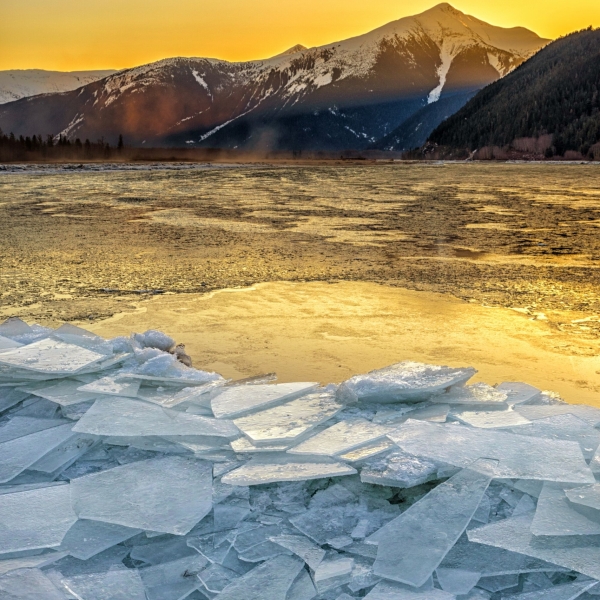 Thin squares of ice sit piled up on the surface of a lake at sunrise, mountains in the background.