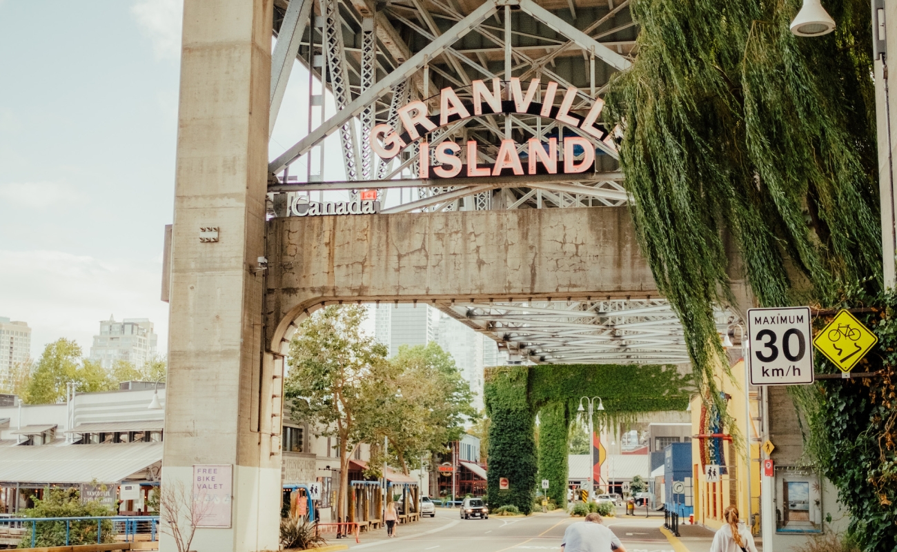 People walking and cycling under a bridge toward a sign that reads 