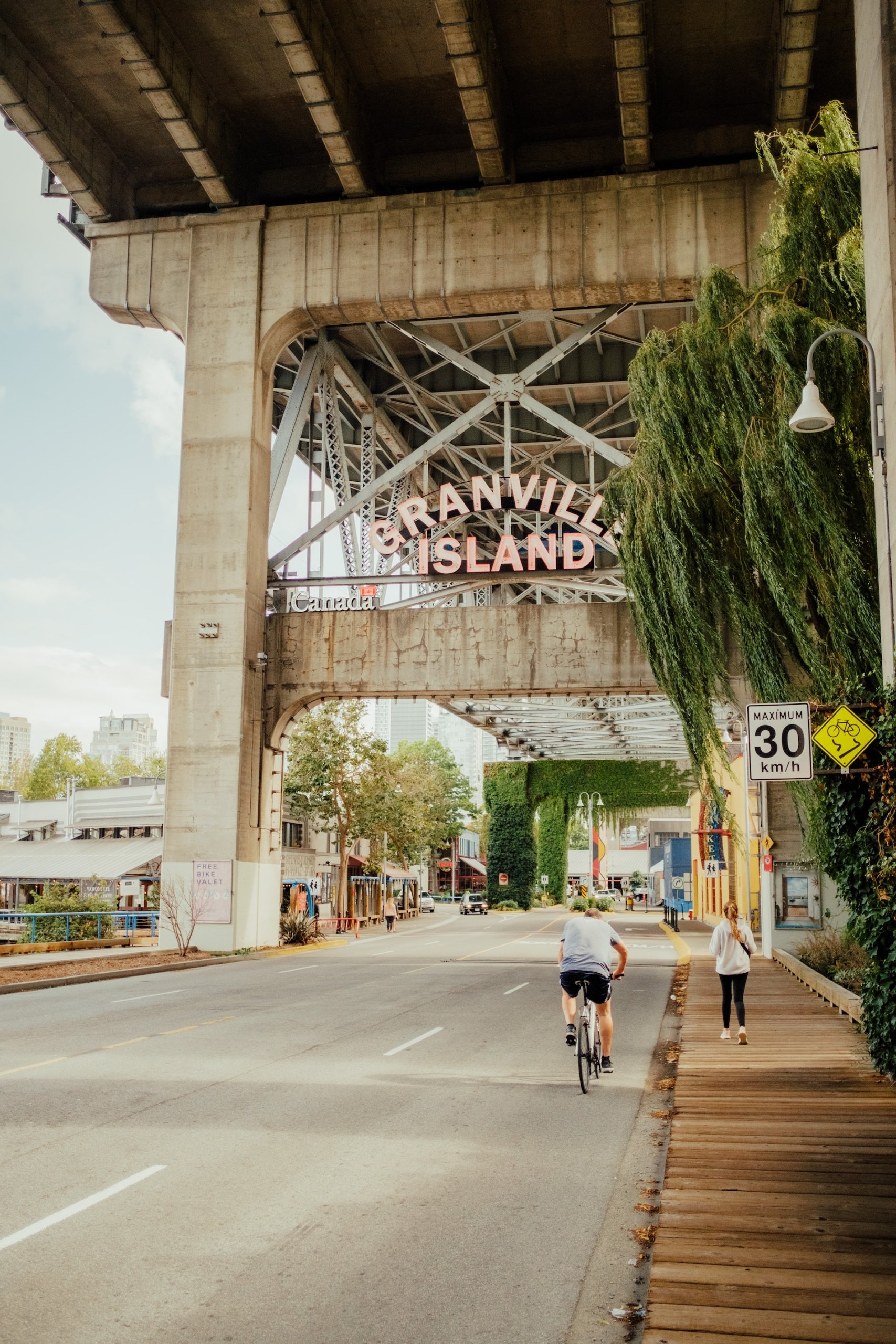 People walking and cycling under a bridge toward a sign that reads 