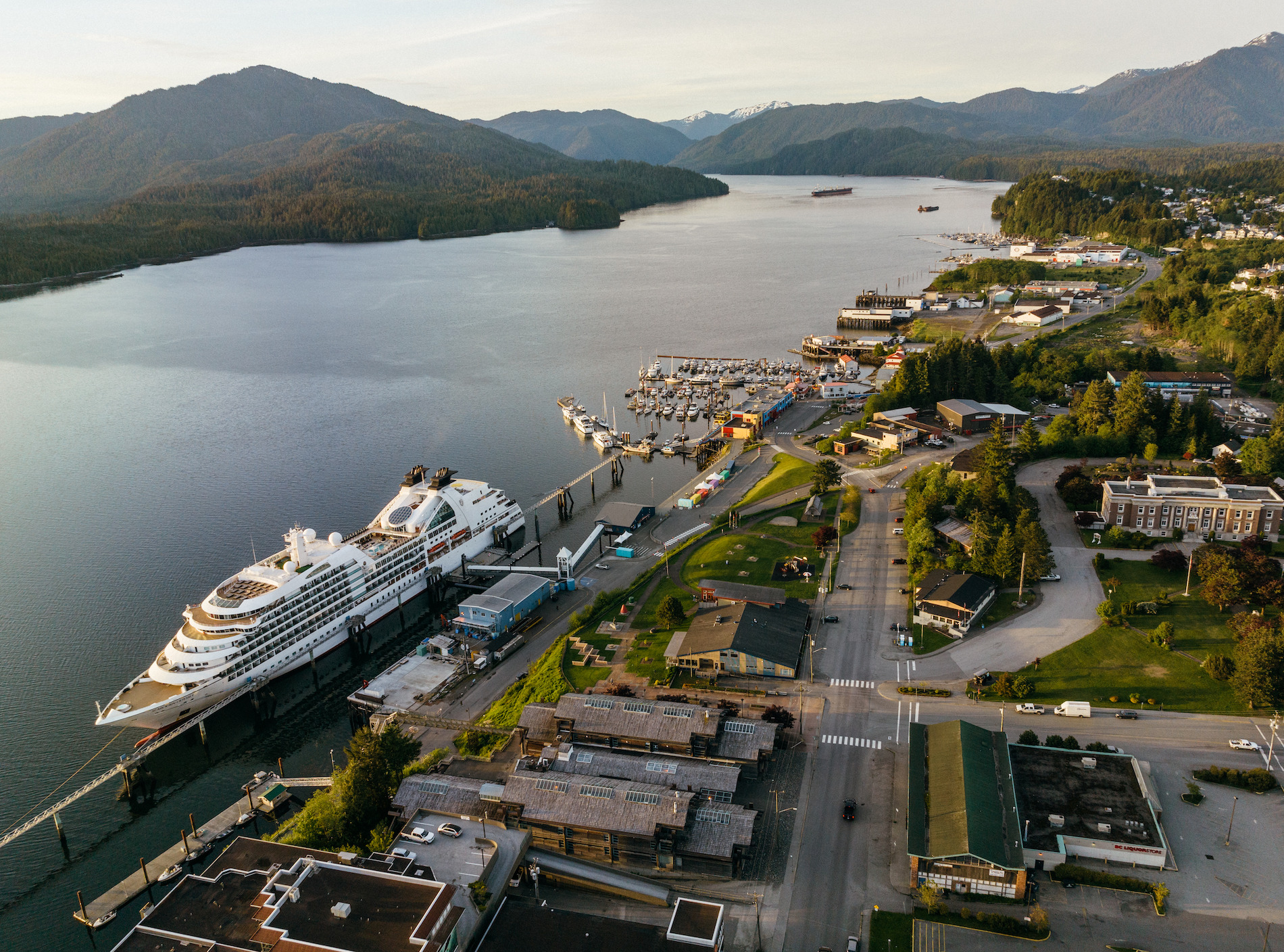 An aerial view of a cruise ship docked at the harbour in Prince Rupert with the Pacific Ocean and mountains in the background.