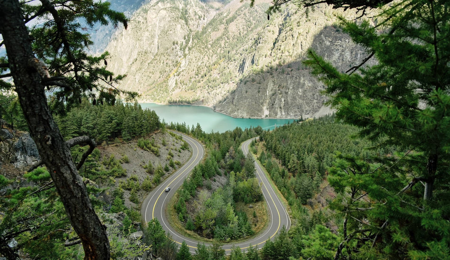 View toward a turquoise lake with a forested landscape in the foreground and sagebrush-covered mountains in the background.