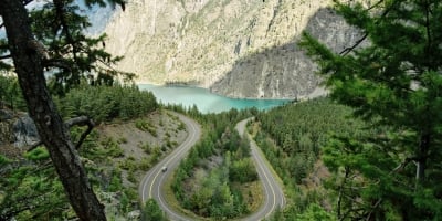 View toward a turquoise lake with a forested landscape in the foreground and sagebrush-covered mountains in the background.