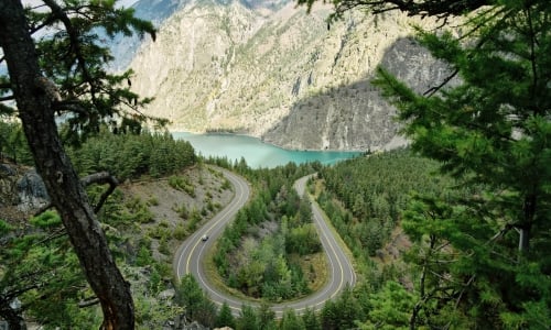 View toward a turquoise lake with a forested landscape in the foreground and sagebrush-covered mountains in the background.
