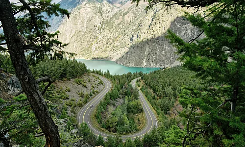 View toward a turquoise lake with a forested landscape in the foreground and sagebrush-covered mountains in the background.