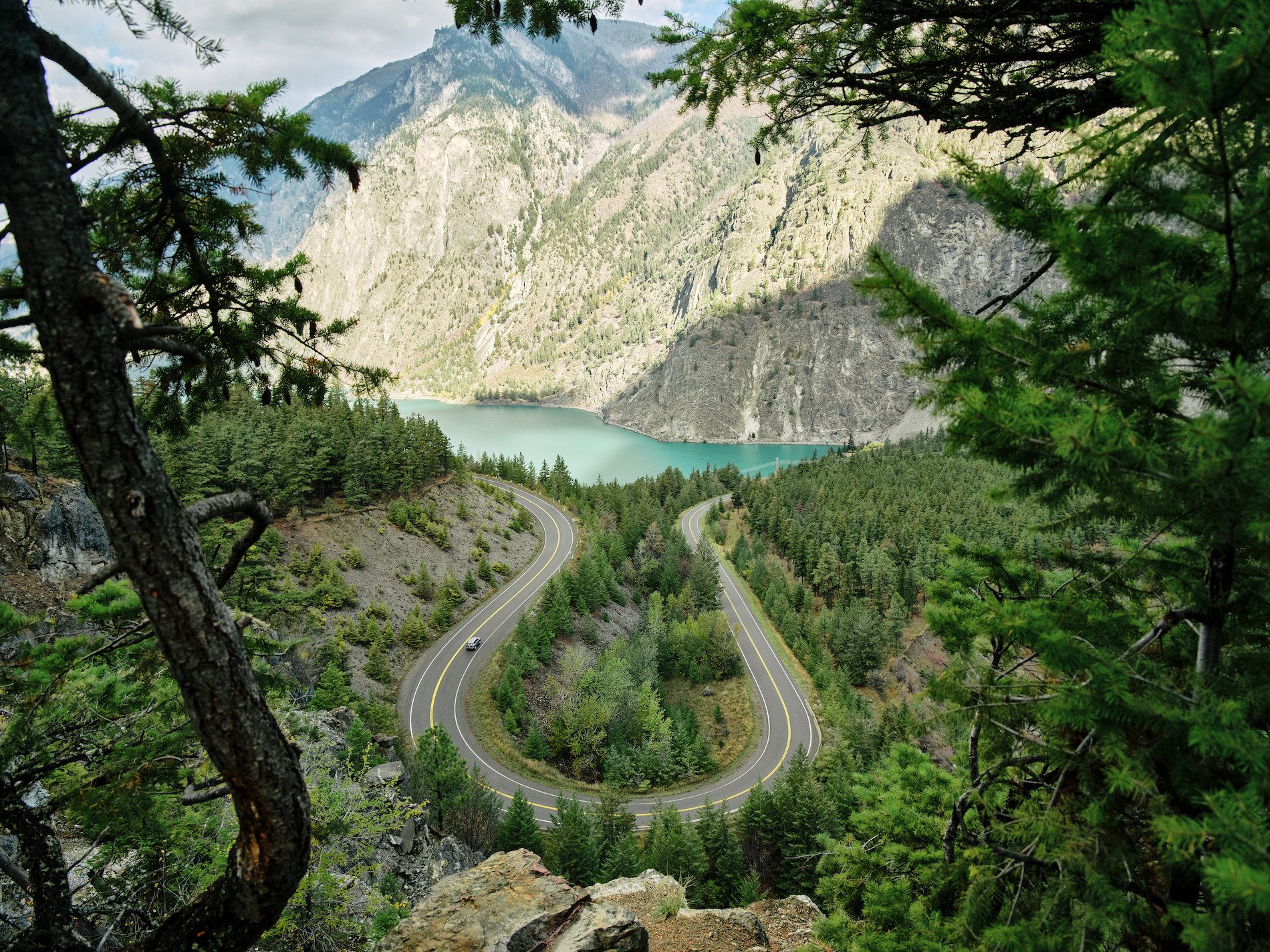 View toward a turquoise lake with a forested landscape in the foreground and sagebrush-covered mountains in the background.