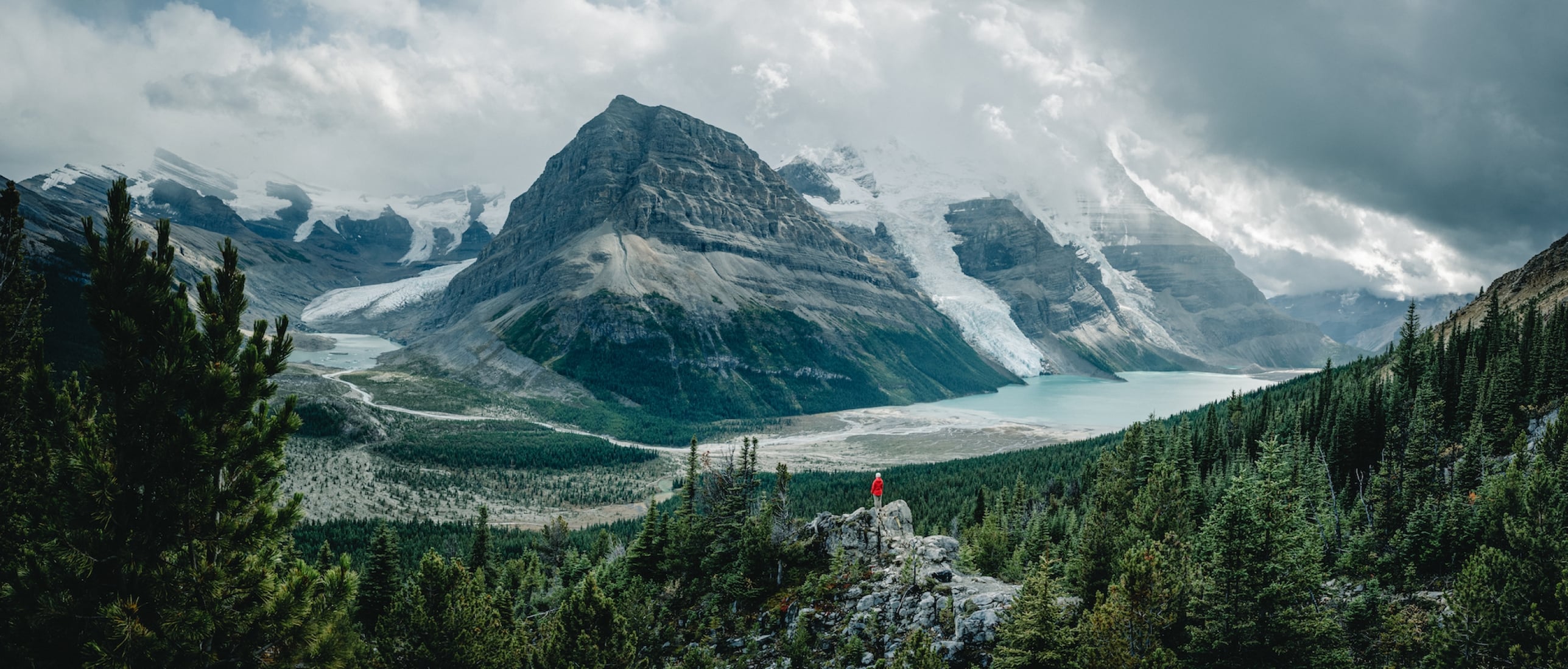 A person is perched overlooking the towering peaks and large glaciers of Mt. Robson.