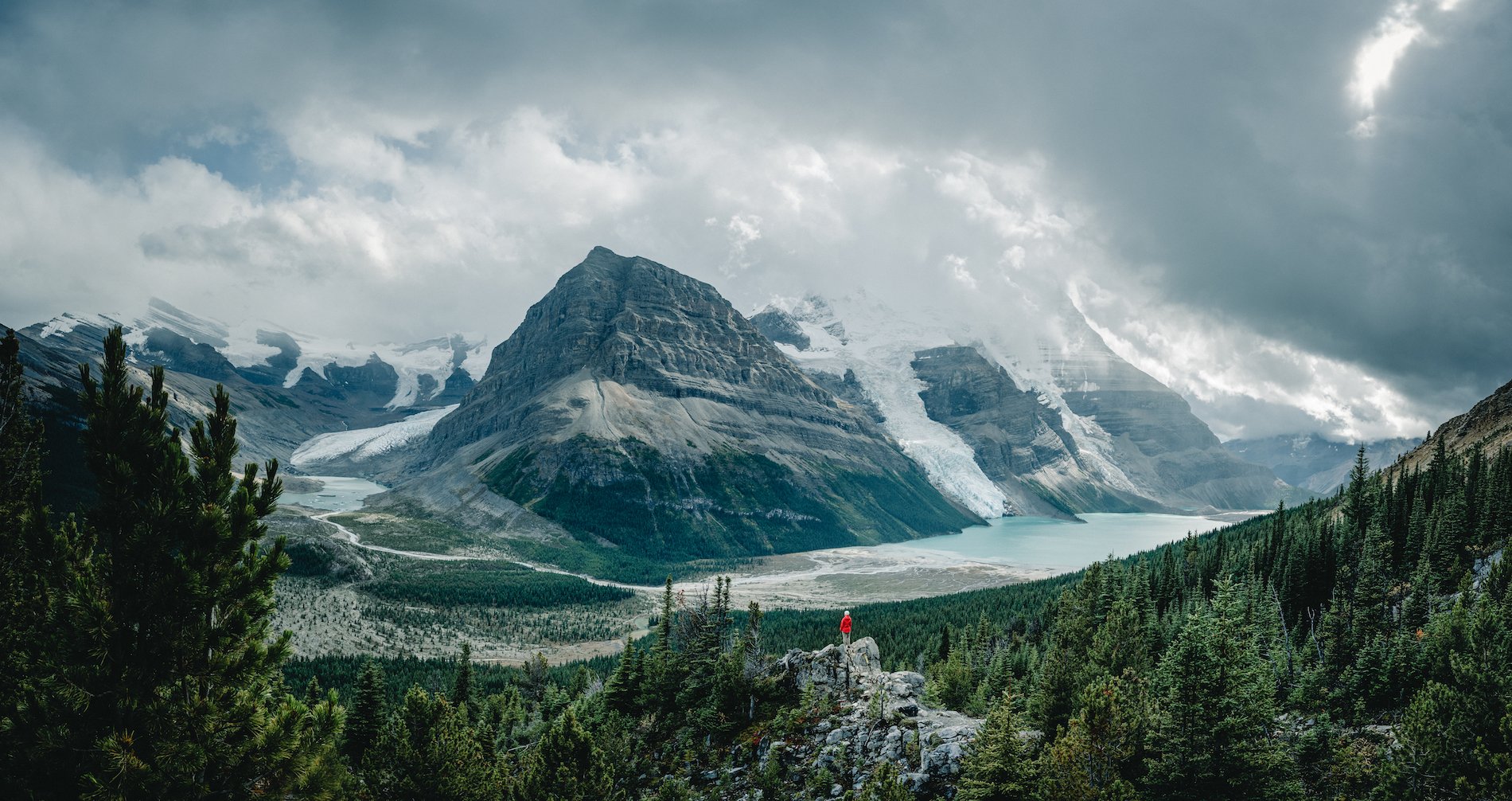 A person is perched overlooking the towering peaks and large glaciers of Mt. Robson.