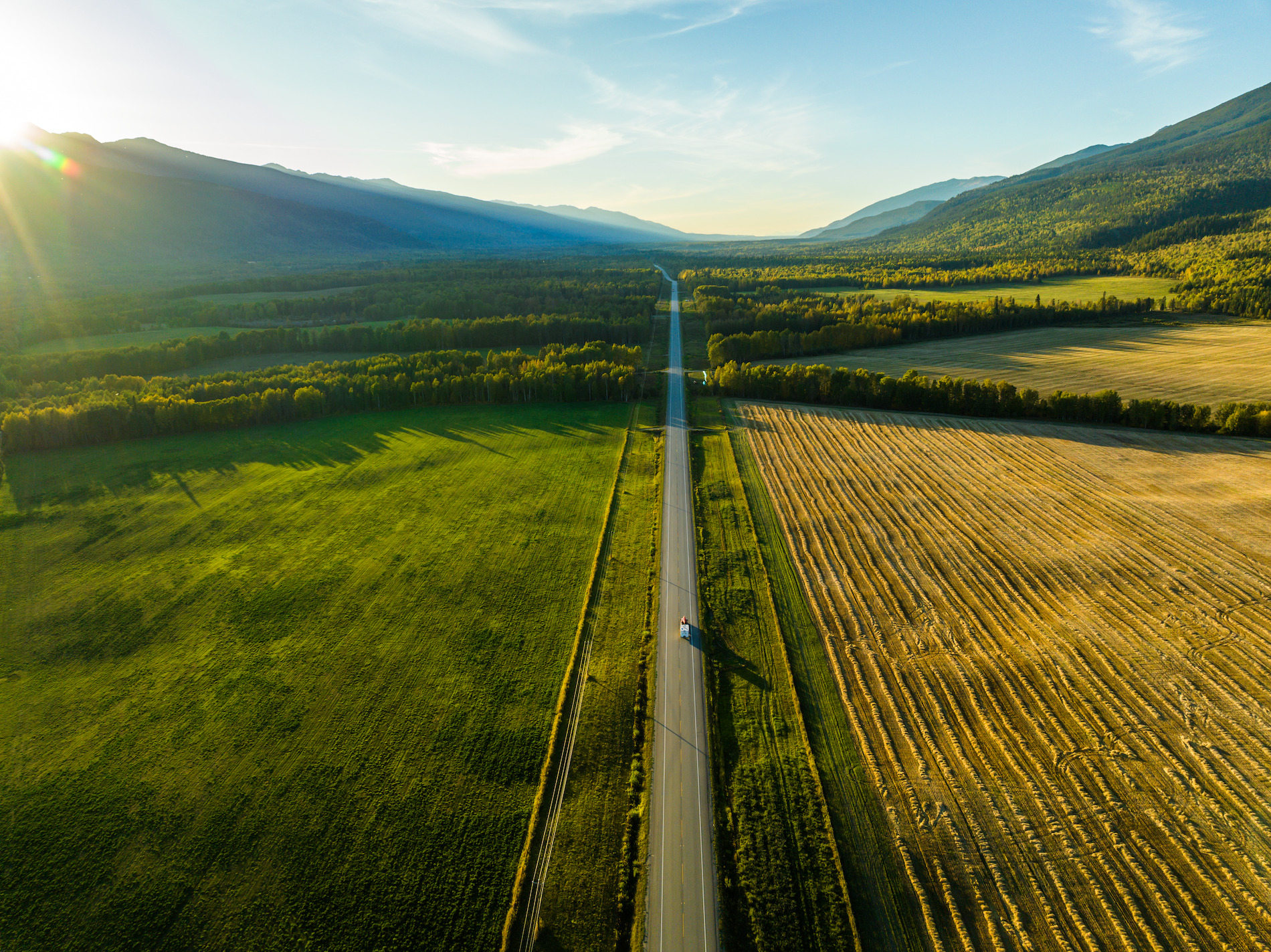 A car driving along a road by farm land