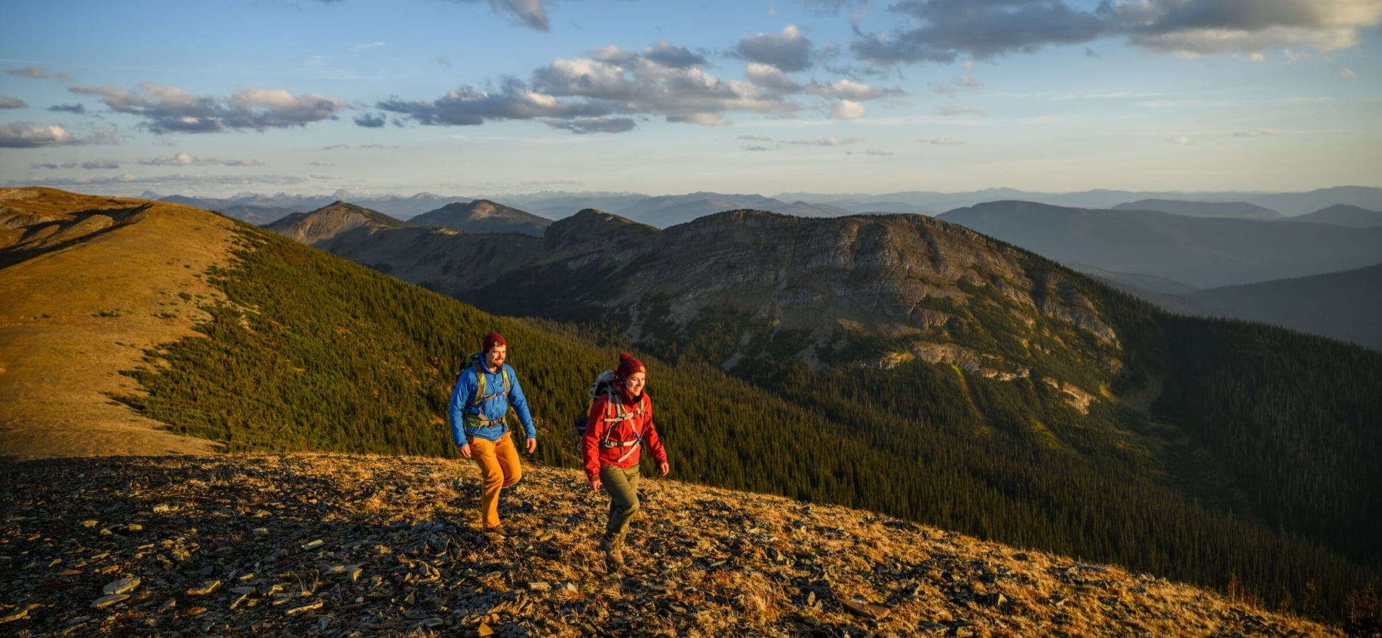 A couple hikes along a mountain ridge with vast range extends into the background.