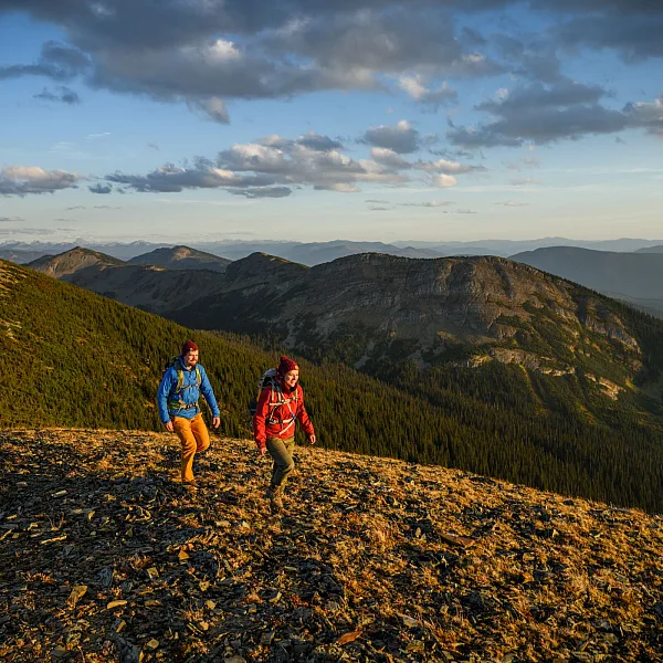 A couple hikes along a mountain ridge with vast range extends into the background.