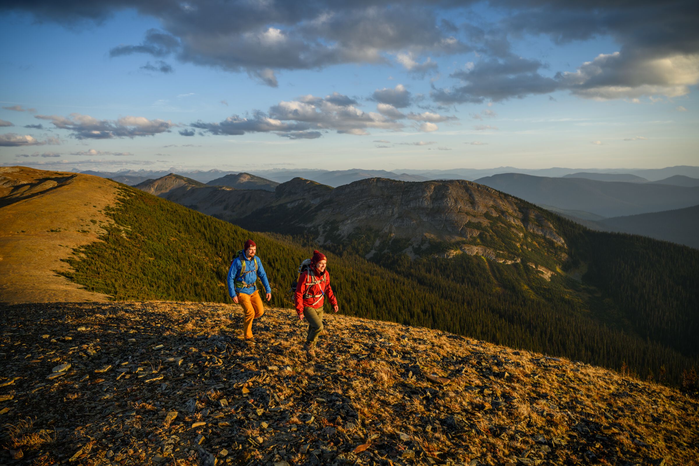 A couple hikes along a mountain ridge with vast range extends into the background.