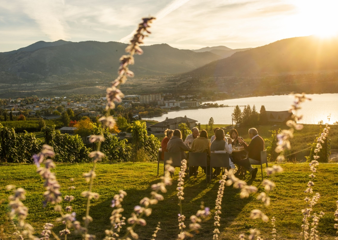 Family and friends dining outdoors at Poplar Grove Winery in Penticton with Okanagan Lake in the background.