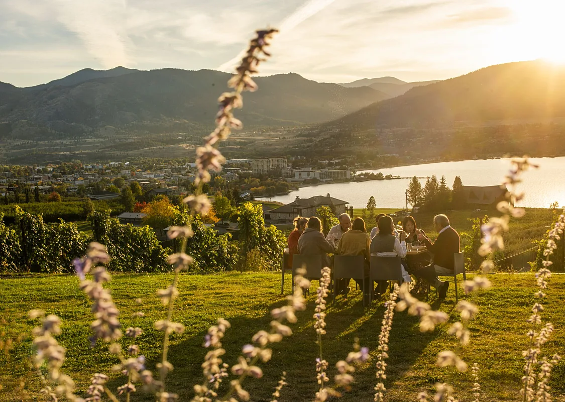 Familiares y amigos cenando al aire libre en Poplar Grove Winery en Penticton con el lago Okanagan al fondo.