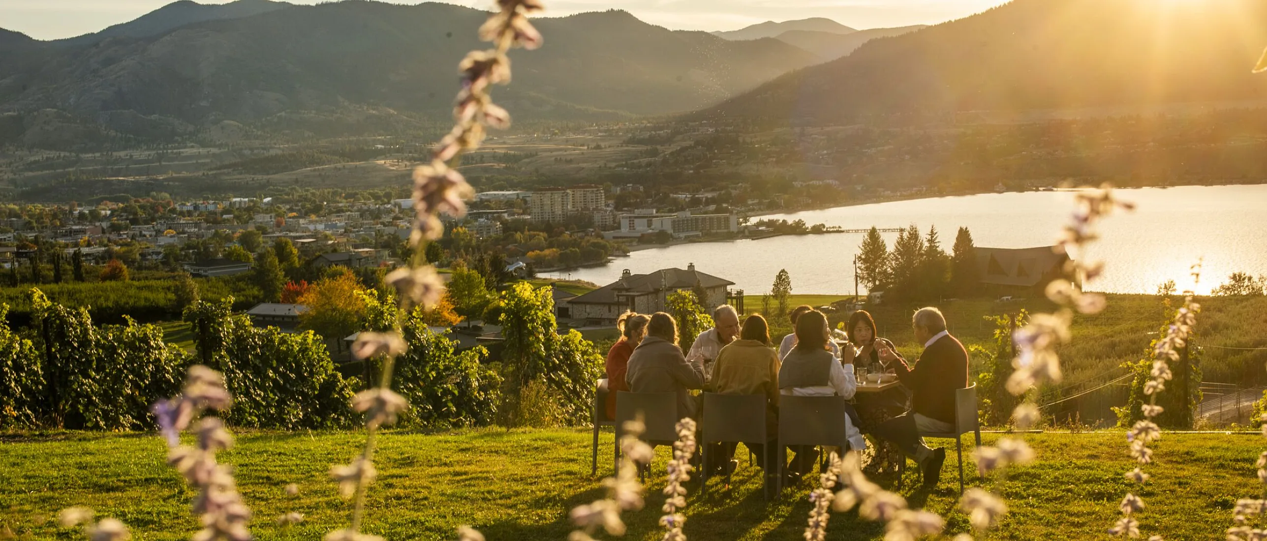 Family and friends dining outdoors at Poplar Grove Winery in Penticton with Okanagan Lake in the background.