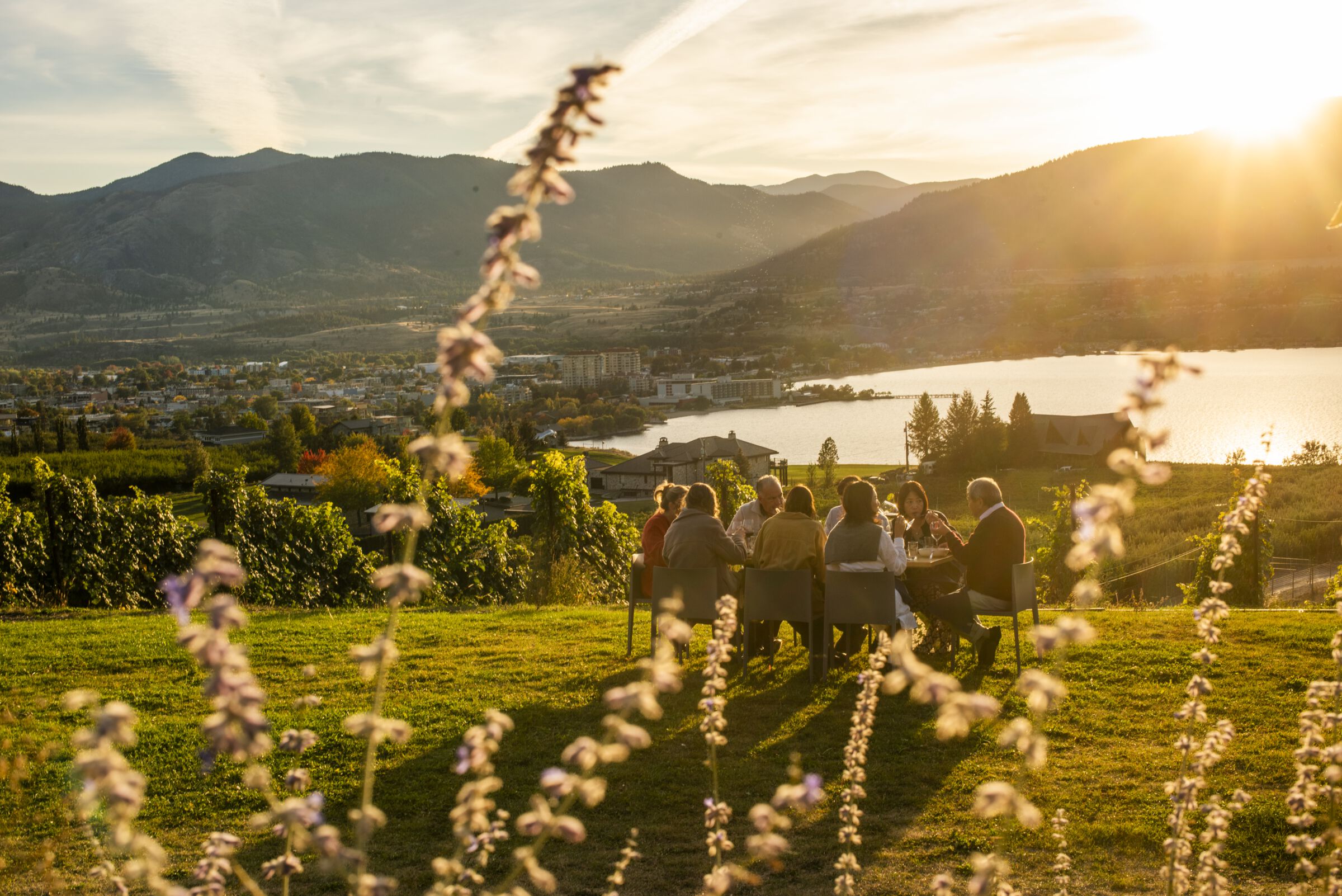Family and friends dining outdoors at Poplar Grove Winery in Penticton with Okanagan Lake in the background.