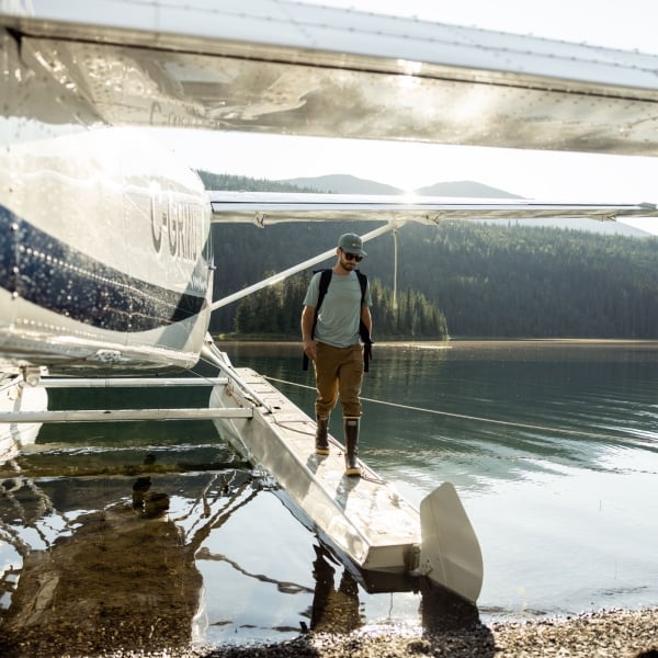 Eine Person mit Rucksack und Wanderkleidung steigt aus einem Wasserflugzeug, das auf einem Bergsee gelandet ist.