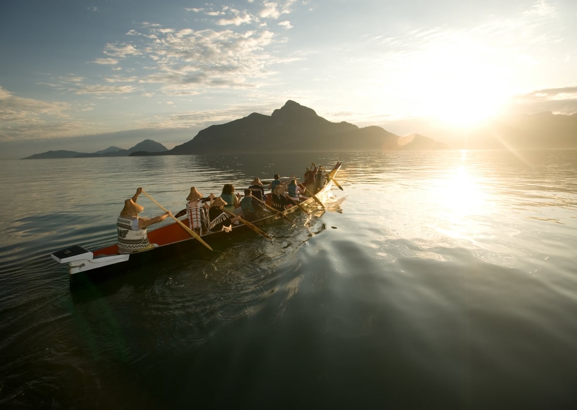 Eine Gruppe rudert mit Takaya Tours ein traditionelles Kanu der First Nations im Howe Sound mit Bergen im Hintergrund.