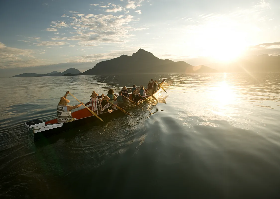 A group with Takaya Tours, rowing a traditional First Nations canoe in Howe Sound with mountains in the background.