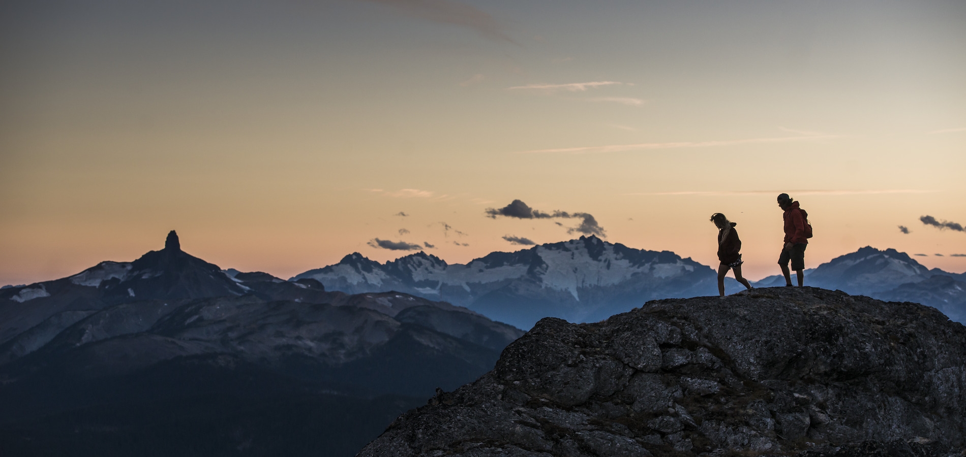 Zwei Wander*innen stehen bei Sonnenuntergang auf dem High Note Trail. In der Ferne ist Black Tusk zu sehen.