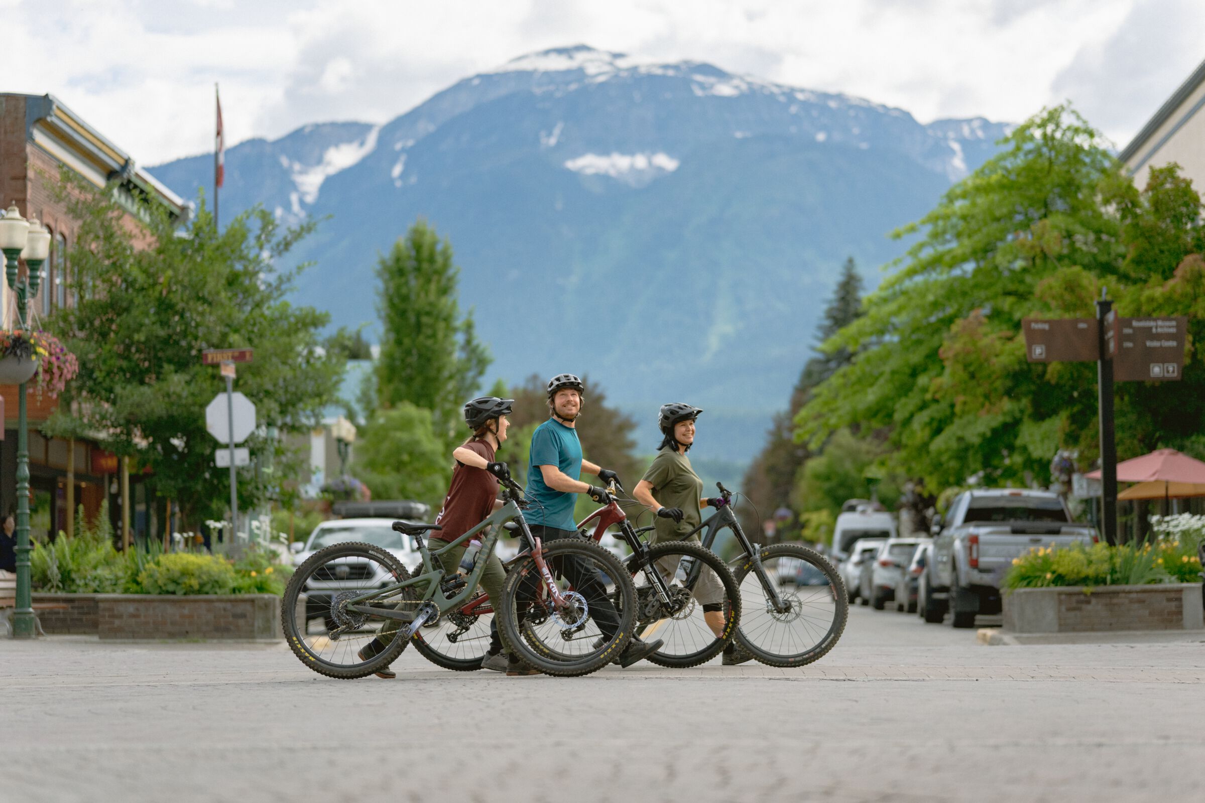 Three friends walking their bikes across the street during their bike ride in downtown Revelstoke.