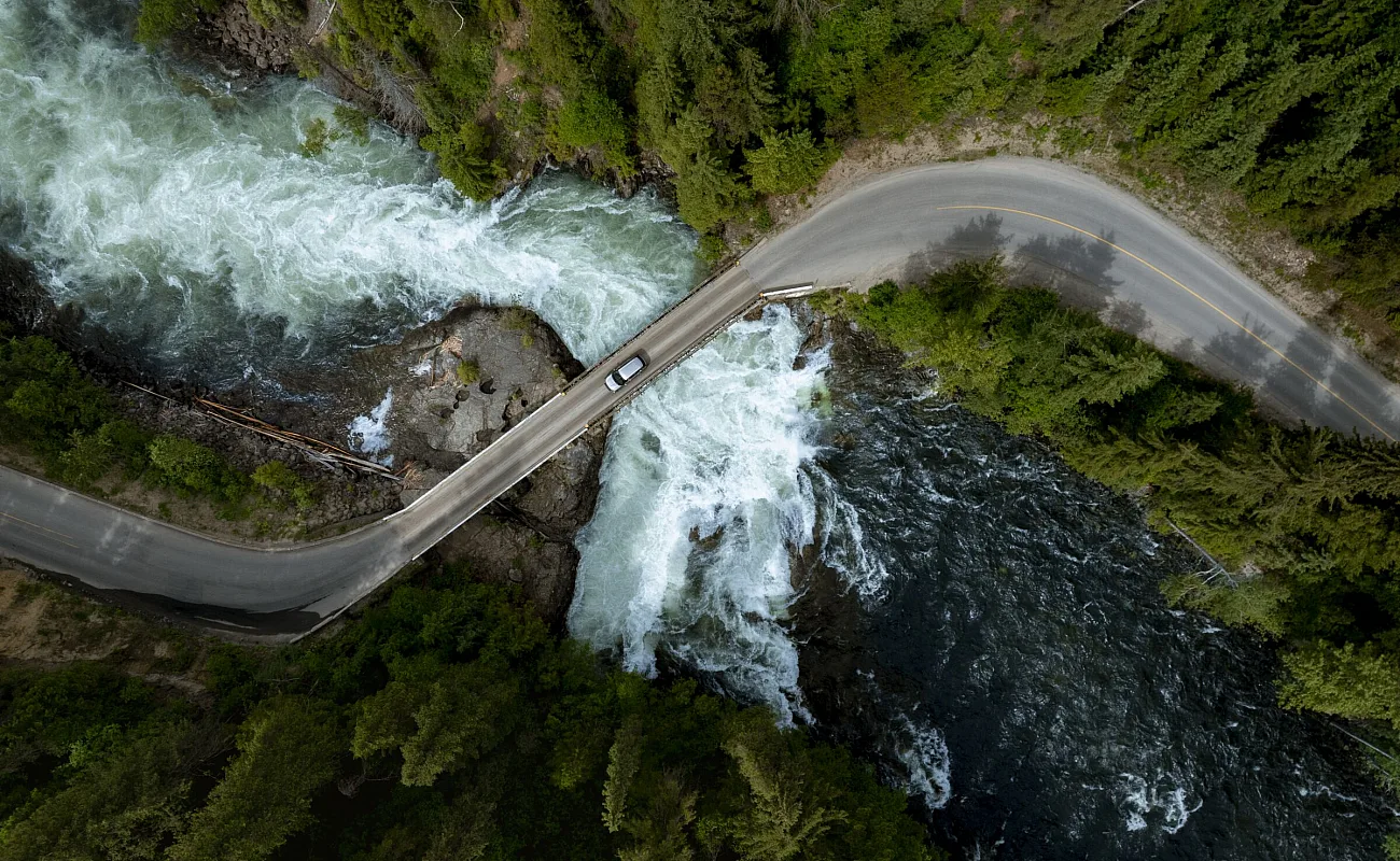An aerial view of a car driving across a bridge at the Mushbowl, a small waterfall sandwiched in between the two mammoth cataracts of the Murtle River, Helmcken Falls and Dawson Falls, in Wells Gray Provincial Park.