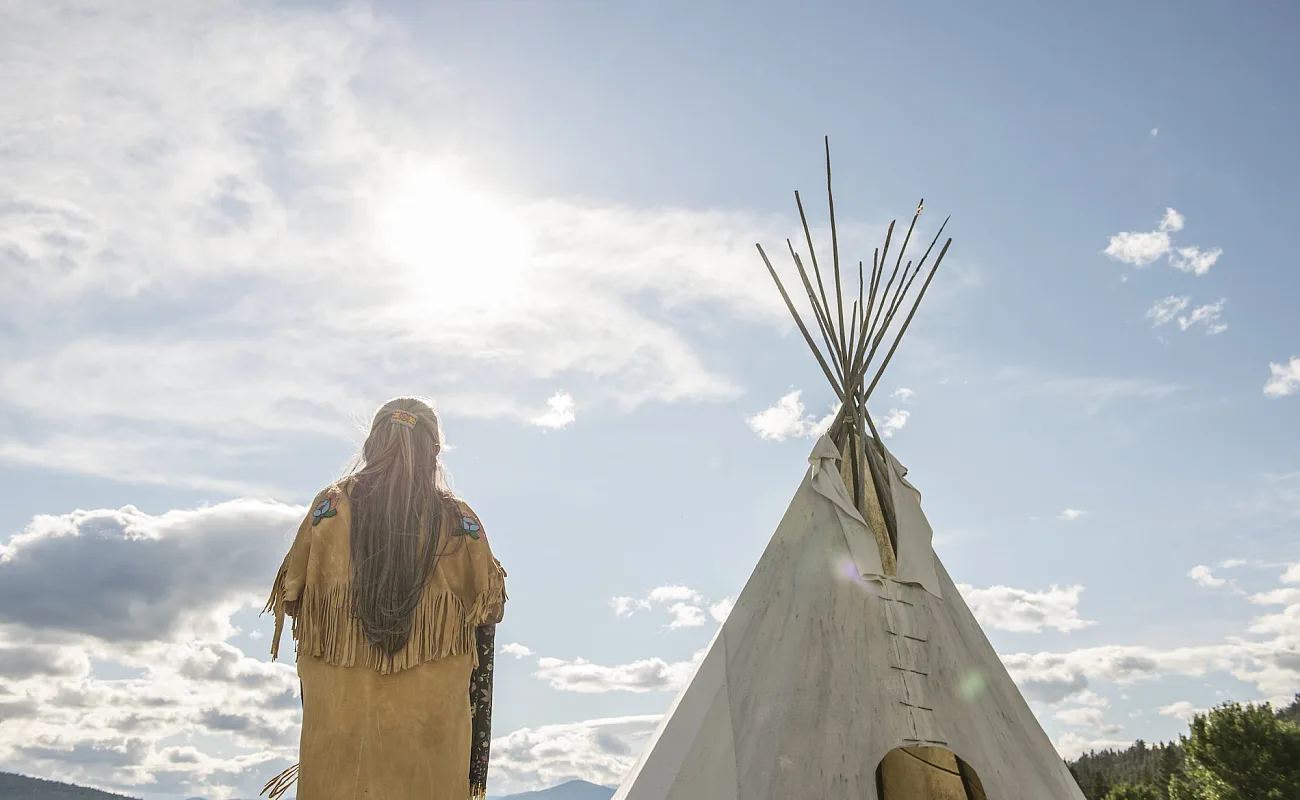 Ktunaxa-Älteste*r in traditioneller Kleidung neben einem Tipi im St Eugene Golf Resort.
