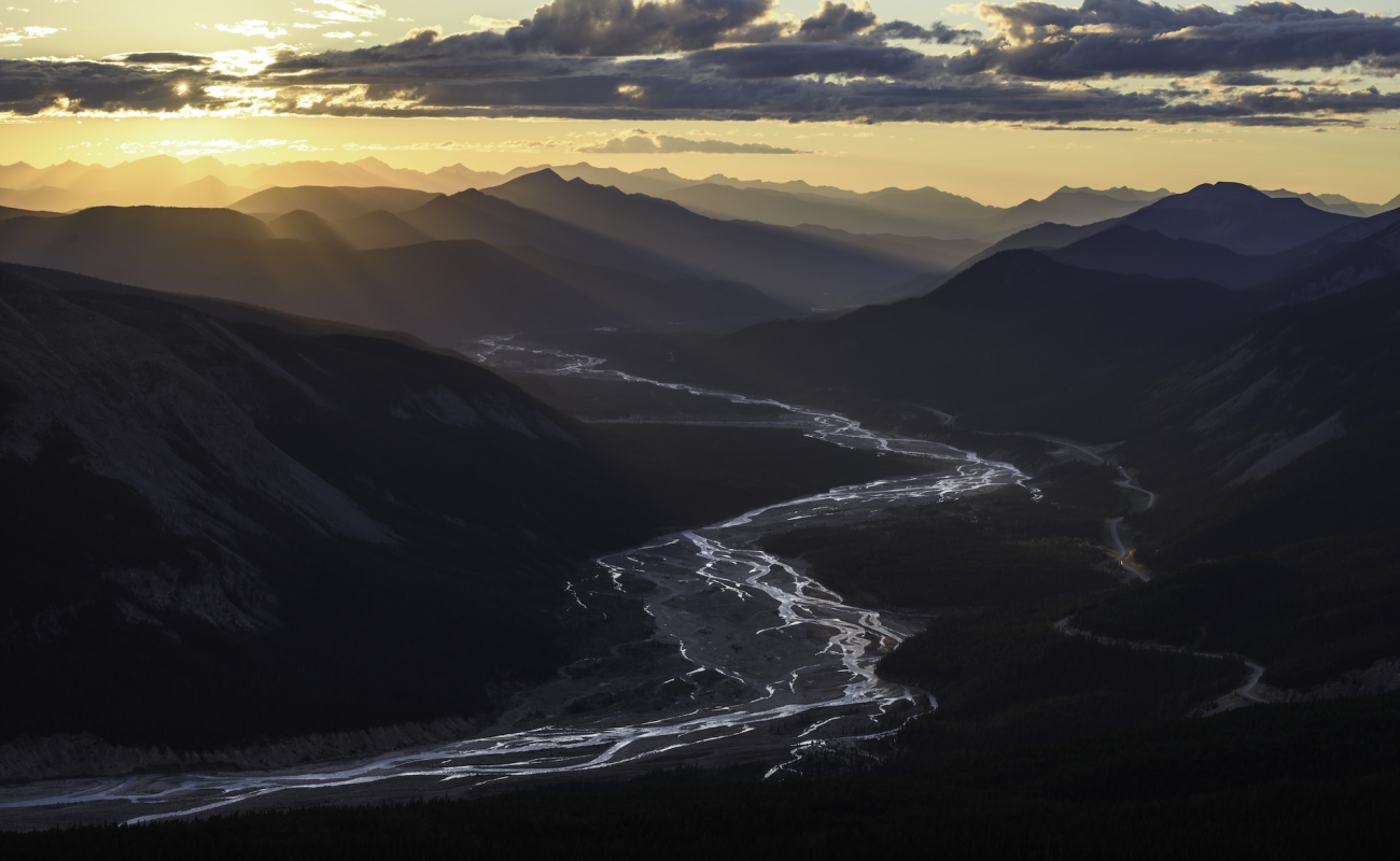Vibrant rays of sun shine down on a mountain river valley in Stone Mountain Provincial Park.