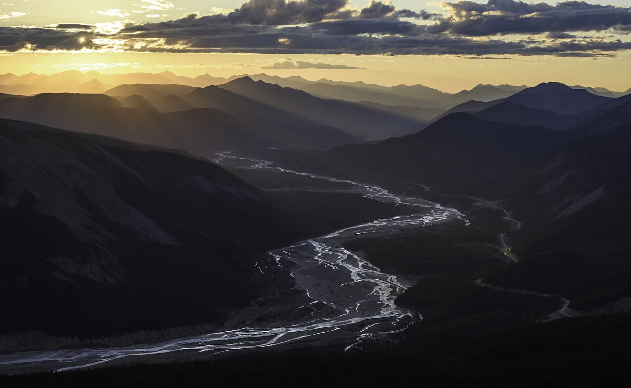 Vibrantes rayos de sol iluminan un valle de río de montaña en Stone Mountain Provincial Park.