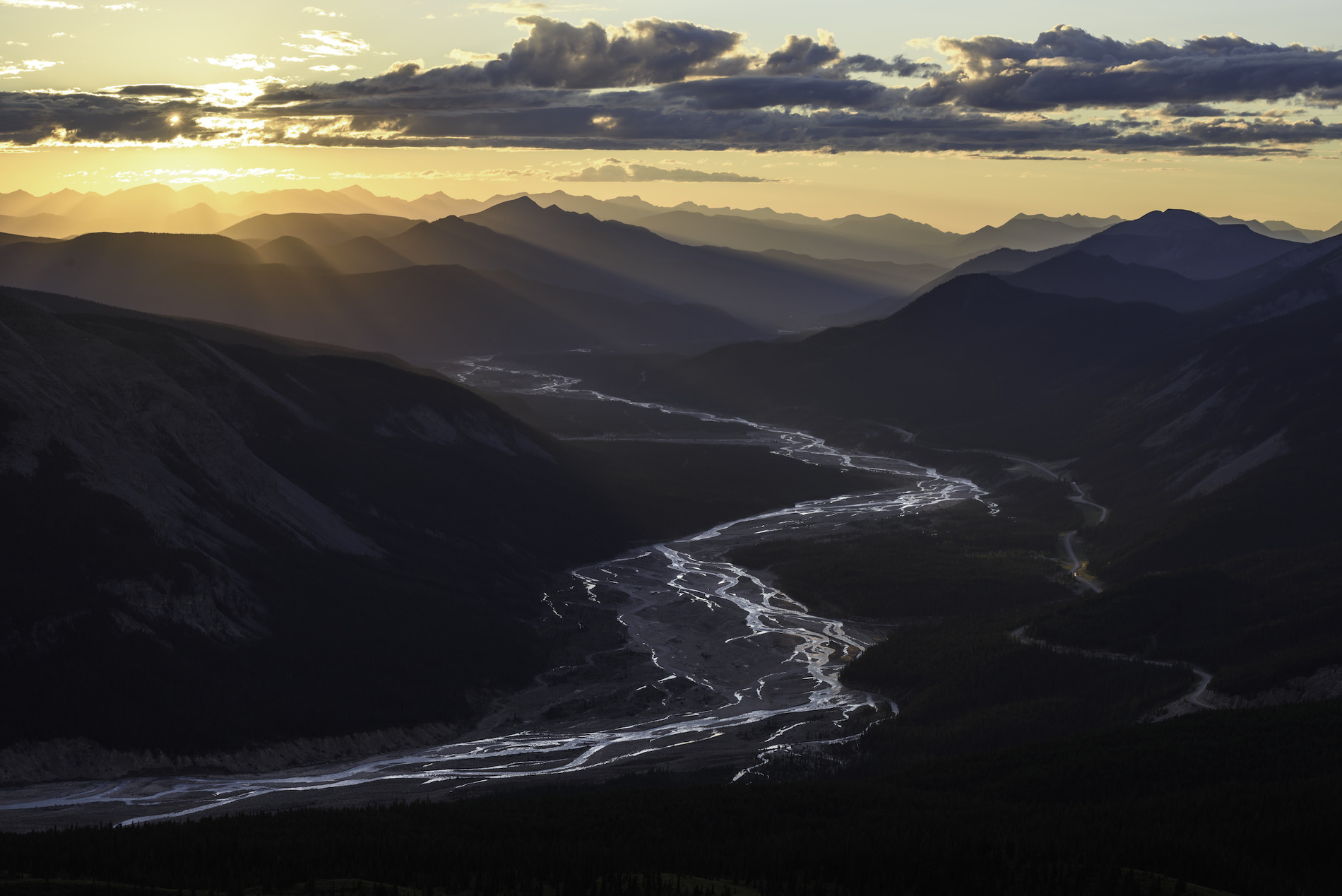 Vibrant rays of sun shine down on a mountain river valley in Stone Mountain Provincial Park.