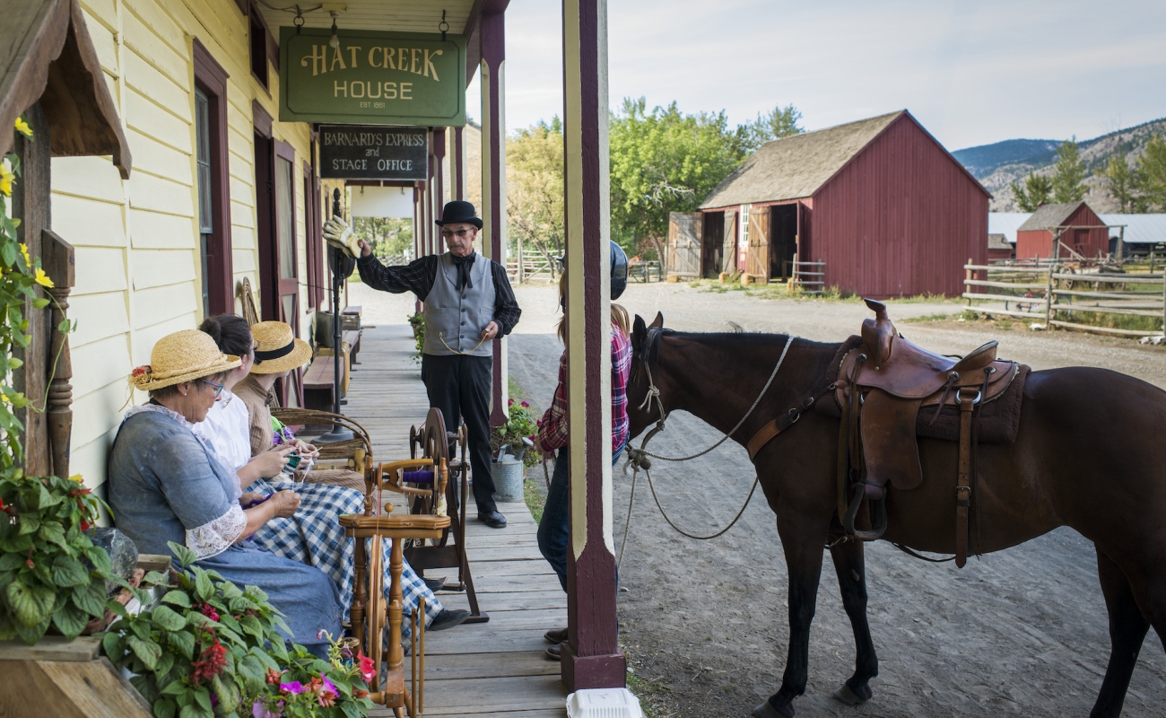 Actores con vestuario histórico se sientan afuera en una banca en Hat Creek Ranch. Un caballo está atado al edificio.