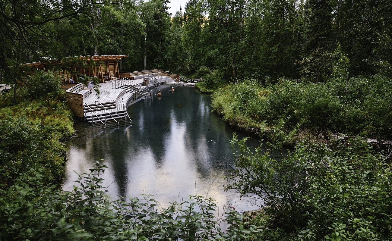 People soaking in the Liard River Hot Springs, mineral baths surrounded by lush forest.