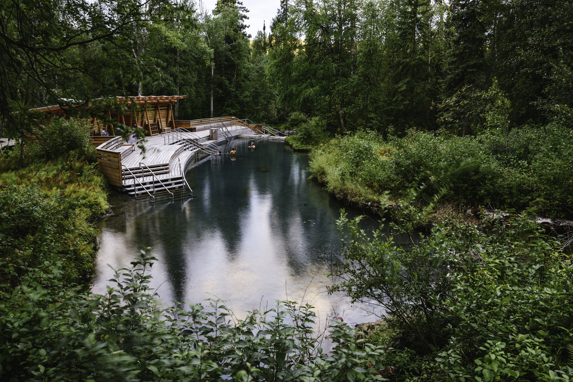 People soaking in the Liard River Hot Springs, mineral baths surrounded by lush forest.