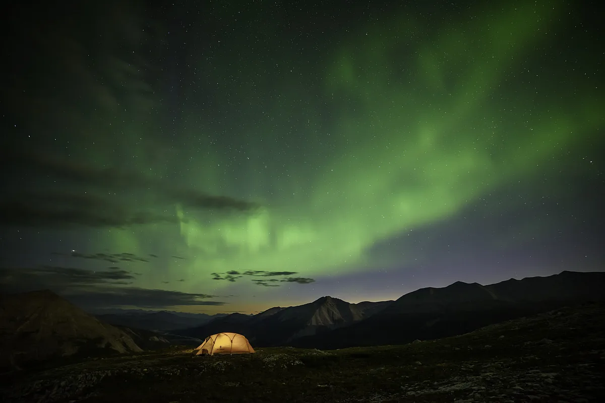 An illuminated tent under the Northern Lights.
