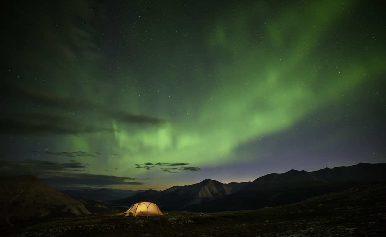 An illuminated tent under the Northern Lights.