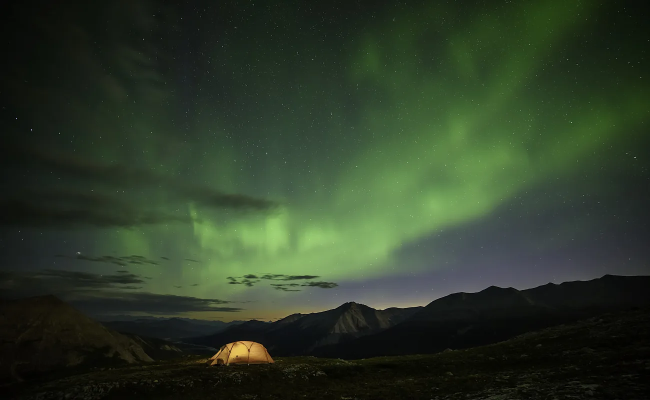 An illuminated tent under the Northern Lights.