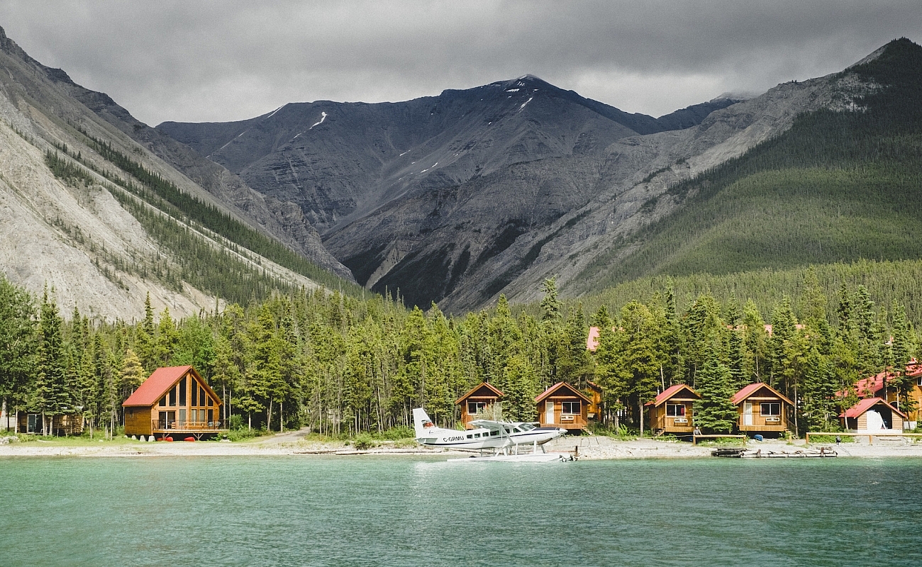 Northern Rockies Lodge with small lakeside cabins, views of the mountains and a float plane parked out front.