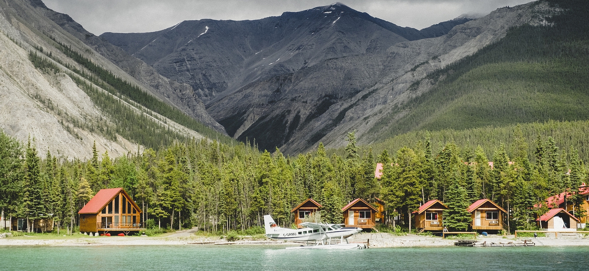 Northern Rockies Lodge with small lakeside cabins, views of the mountains and a float plane parked out front.
