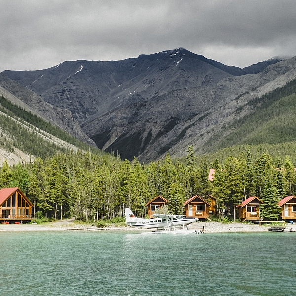 Northern Rockies Lodge with small lakeside cabins, views of the mountains and a float plane parked out front.