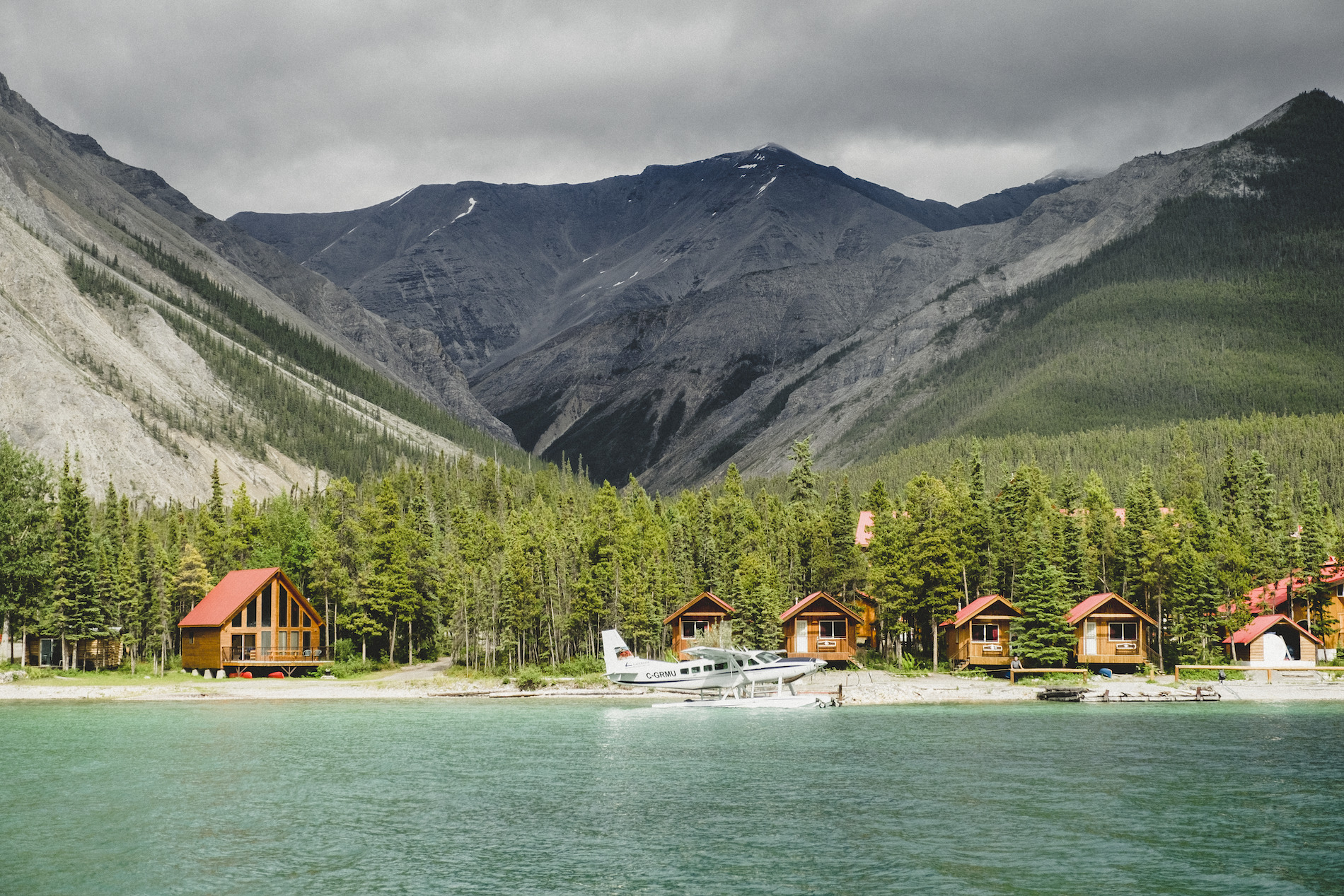 Northern Rockies Lodge with small lakeside cabins, views of the mountains and a float plane parked out front.