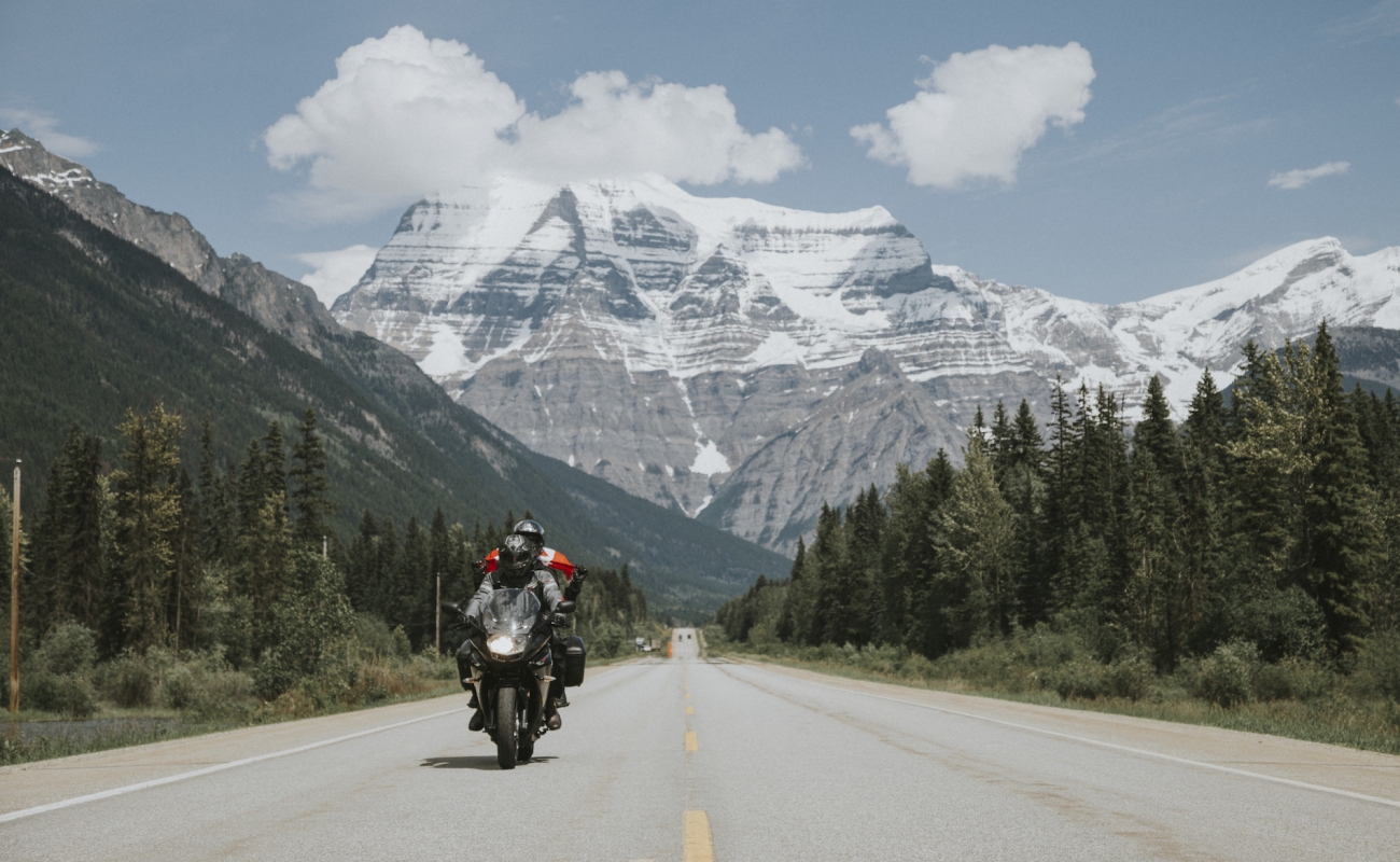 Una motocicleta con dos personas en la carretera con el imponente Mount Robson de fondo.