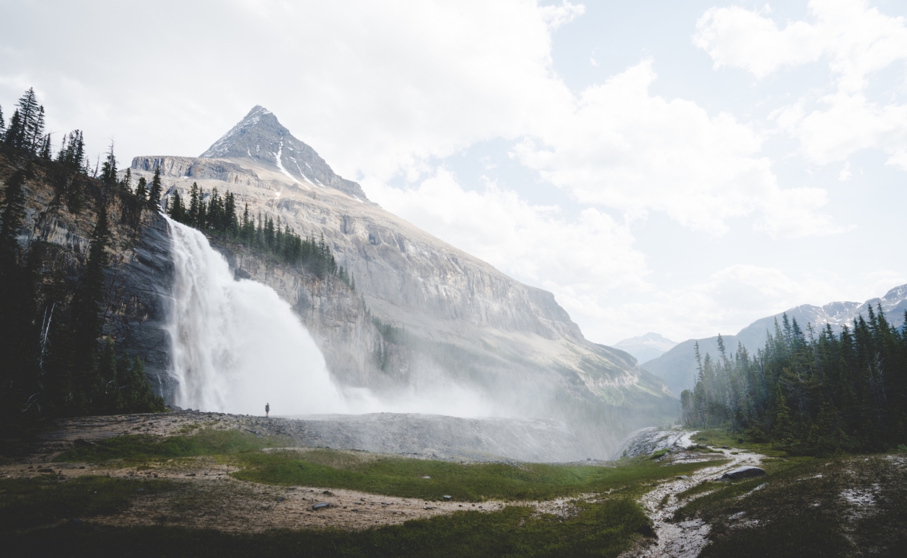 A person in the distance stands in front of Emperor Falls on the Berg Lake Trail