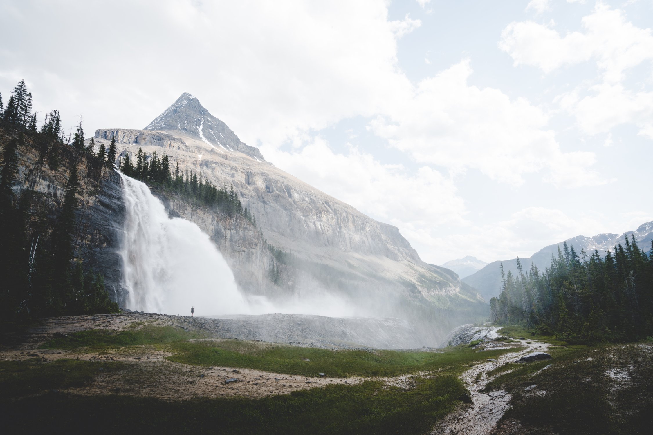 A person in the distance stands in front of Emperor Falls on the Berg Lake Trail