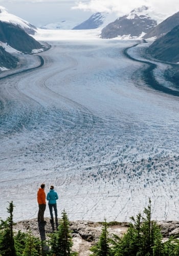 Dos personas contemplan un paisaje congelado en la región de Stewart-Cassiar, al norte de BC. Están de pie en un promontorio rocoso y miran hacia la cordillera.