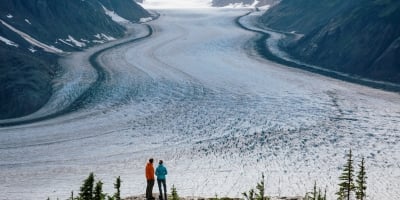 Two people look out at a frozen landscape in the Stewart-Cassiar region of northern BC. They stand on a rocky outcrop and are looking towards the mountain range.