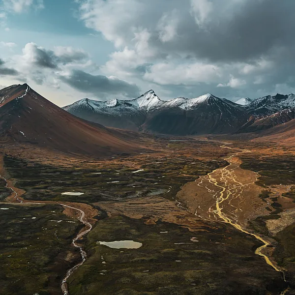 An aerial view of a vast landscape with mineral-streaked orange mountains and a lush river valley below.